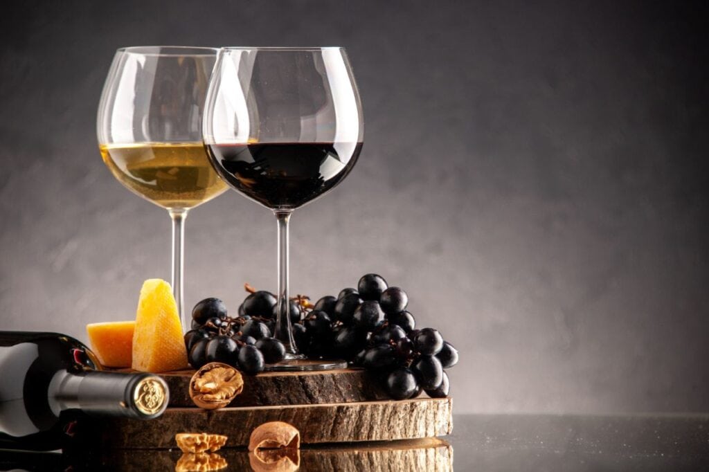 front view wine glasses fresh grapes walnuts yellow cheese wood board overturned bottle dark background